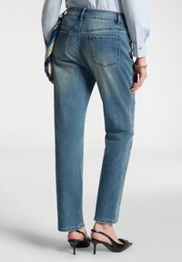 Jeans in denim blu con un design a gamba dritta, caratterizzati da una vita media e tasche posteriori, abbinati a scarpe con tacco nere.