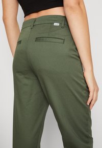 Pantalon vert olive en tissu lisse, avec une coupe droite, des poches arrière et une petite étiquette logo Levi's près de la taille.