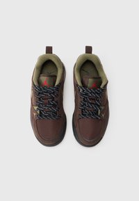 Brune netting og ruskinds sneakers med sort og hvit mønstrede snørebånd, grønne detaljer, elliptisk form og rød logo på tungen.