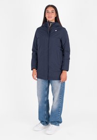 Mornarsko modra insulated parka jakna z zadrgo spredaj, dvema stranskima žepoma in visokim ovratnikom. Ustrezno kombinirana z ravnimi svetlo modrimi kavbojkami.