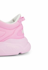 Talons de baskets de sport roses avec semelle texturée, dessus en tissu, languette de tirage, marqués "HUGO" sur la semelle et à l'arrière, doublure intérieure blanche visible.