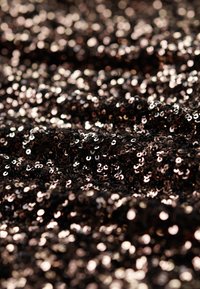 Czarna tkanina pokryta migoczącymi cekinami o różnych rozmiarach, odbijająca światło w mieszance ciemnych i metalicznych tonów na teksturowanej powierzchni.
