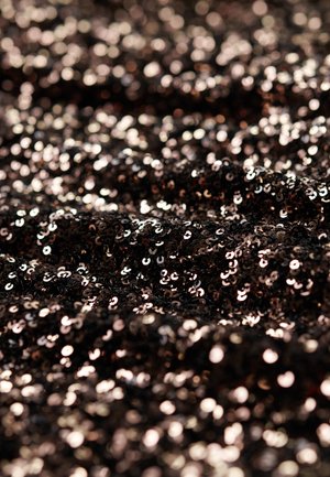 Tejido negro cubierto de brillantes lentejuelas de tamaños variados, que reflejan la luz con una mezcla de tonos oscuros y metálicos en una superficie texturizada.