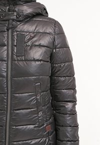 Černá prošívaná péřová bunda s předním zipem, zakrytými knoflíkovými kapsami a vysokým límcem se cvoky.