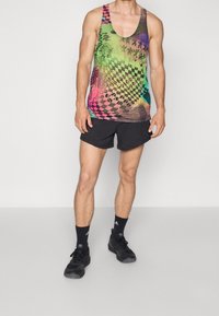 Débardeur multicolore avec un motif à carreaux et des designs ondulés, fabriqué en tissu léger, assorti à un short noir et des chaussures de sport.