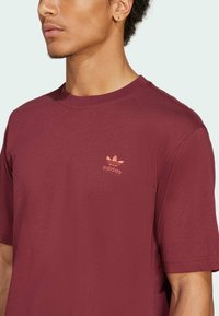 Bordo kratka majica iz mehkega materiala s krožnim izrezom, ki ima na prsih embosirano roza Adidasovo logo.