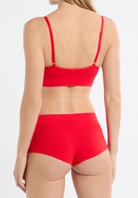 Reggiseno rosso e pantaloncini a vita alta realizzati in materiale a coste. Spalline regolabili e fascia larga in vita con una leggera texture.