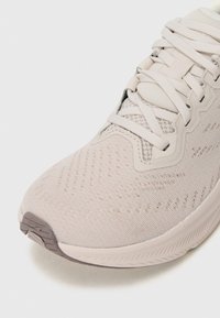 Light beige athletic shoe with a textured knit upper, reinforced toe cap, and flexible sole. Laces are woven through eyelets for secure fit.