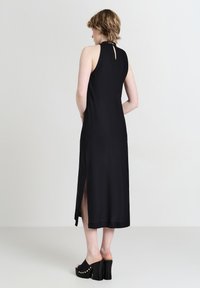 Schwarzes ärmelloses Kleid mit hohem Ausschnitt, das ein Rückenschlüssellochdetail, einen seitlichen Schlitz und einen einfarbigen Stoff aufweist. Trage es mit schwarzen Plateausandalen.