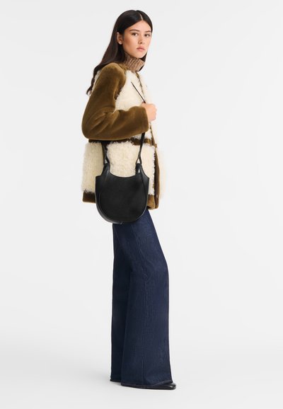 Black leather shoulder bag with textured finish, paired with a brown and white shearling jacket and dark blue flared jeans.