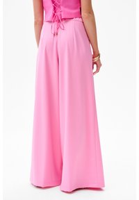 Pantalons palazzo roses en tissu lisse. Comprend une taille haute et une silhouette fluide avec une coupe décontractée. Pas de motifs visibles.
