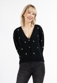 Cardigan nero con scollatura a V profonda e motivo a cuore dorato. Presenta bottoni sul davanti e polsini e orlo a coste. Texture in maglia leggera.