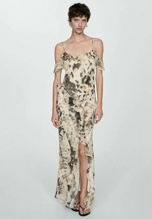 Off-shoulder jurk in beige en donkerbruin abstract patroon. Heeft franjes en een hoge split voor extra detail.