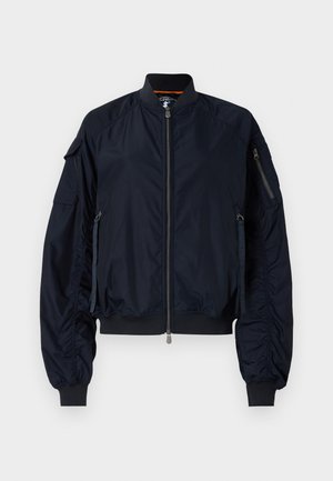 Chaqueta bomber azul marino con cremallera frontal, puños y dobladillo acanalados. Cuenta con múltiples bolsillos con cremallera y detalles fruncidos en las mangas. Textura suave.