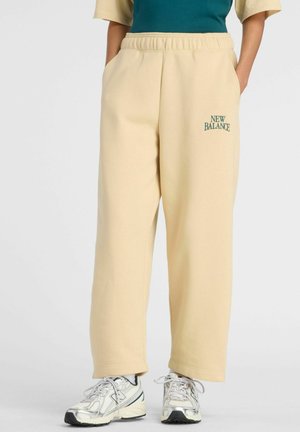 Beige New Balance joggingbukser med elastisk talje og sidelommer, båret med hvide New Balance sneakers.