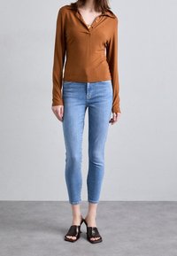 Top de manga larga marrón acanalado con cuello, jeans ajustados azul claro y mule de punta abierta marrones oscuros con acabado texturizado.