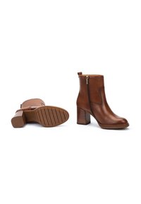 Botines de cuero marrón hasta el tobillo con tacón cuadrado, cremallera lateral y suela texturizada. Presentan un acabado liso y una pequeña lengüeta en la parte trasera.