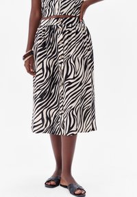 Zebraprint rok in zwart en crème, met een knoopsluiting aan de voorkant, een elastische tailleband en een knielange snit. Gestyled met zwarte instappers.