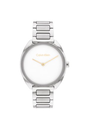 Montre en métal argenté avec un boîtier rond, un cadran blanc, des index et aiguilles dorés, et un bracelet texturé élégant. Logo Calvin Klein affiché.