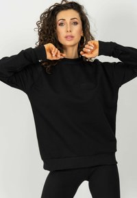 Czarny sweatshirt o prążkowanej strukturze, z okrągłym dekoltem i lekko oversize'owym krojem. Posiada wytłoczone logo z przodu.