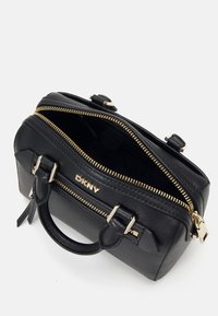 Borsa a mano in pelle nera con finitura texturizzata, zip dorate e dettagli in metallo. Presenta una maniglia superiore e il marchio DKNY sul davanti.