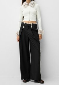 White cropped sweater with fuzzy collar and cuffs; paired with wide-leg black trousers featuring adjustable drawstring waist and side pockets.