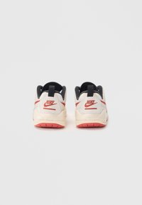 Sneakers Nike, z kremową i czarną cholewką, czerwonymi akcentami i teksturowanym materiałem. Posiadają gumową podeszwę i wyraźne logo.
