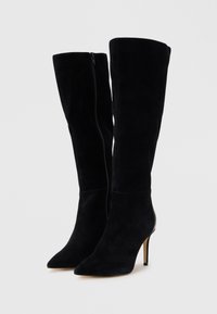 Bottes noires en suede jusqu'au genou avec un bout pointu et un talon aiguille ; elles présentent une fermeture éclair sur le côté et une texture lisse ; silhouette élégante.