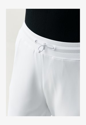 bílé kalhoty s elastickým pasem, vybavené bílým nastavitelným tkaničkovým páskem a sponou, nošené s černým žebrovaným topem.