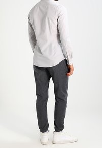 Jasnoszara koszula na guziki z plisą z tyłu, w połączeniu z ciemnoszarymi spodniami i białymi trampkami, widziana od tyłu.