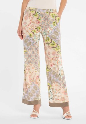 Florale und geometrische Patchwork-Hosen mit weitem Bein in Pastelltönen und beigen Bündchen, getragen mit weißen, mit Riemchen versehenen Sandaletten mit Absatz.