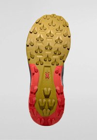 Terränglöpningsskos sula med ett mångriktat mönster för bra grepp. Huvudfärgen är gul med röda accenter och strukturerade skåror för extra fäste.