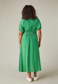 Grön maxiklänning med vita prickar, smockad byst, puffärmar och en svävande kjol. Bärs med vita skor.