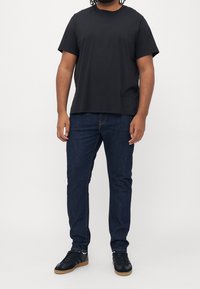 Černé bavlněné tričko s krátkými rukávy, doplněné tmavě modrými džínami. Outfit je doplněn černými teniskami s nazlátlými podrážkami.