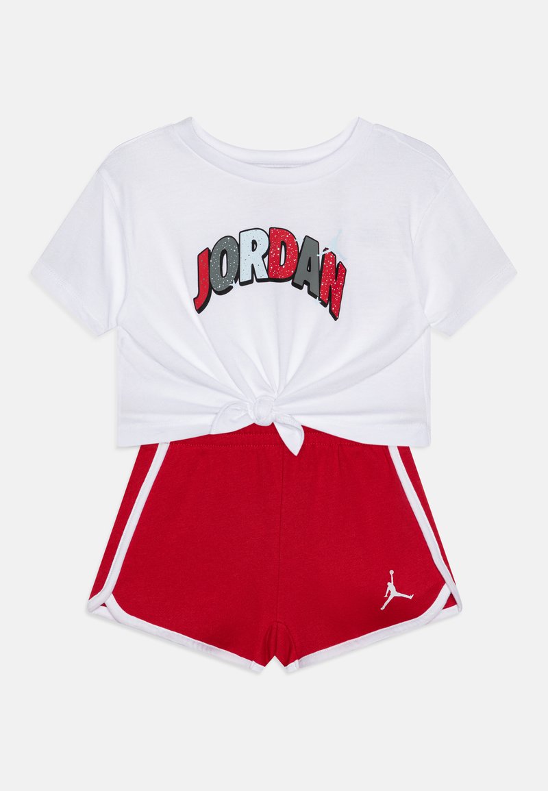 Top corto bianco con "JORDAN" in colori vivi, abbinato a pantaloni corti rossi con strisce laterali bianche e un piccolo logo bianco sull'orlo.