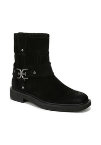 Stivale alla caviglia in suede nero con punta rotonda, cinturino decorativo e fibbia argentata, suola piatta bassa e cuciture bianche in contrasto.