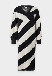 Robe en maille avec un col en V, des manches longues et de larges rayures diagonales noires et crème sur une texture douce.