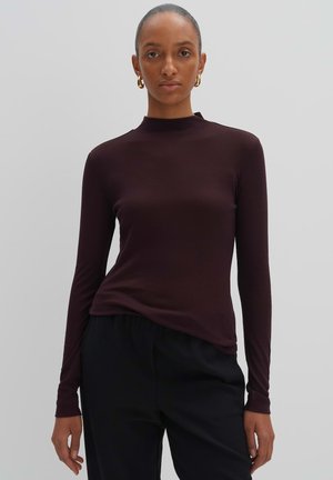 Dunkelburgunderfarbener Langarm-Top mit tailliertem Design und hohem Kragen. Weicher, glatter Stoff und schmale Ärmel. Kombiniert mit schwarzen Hosen.