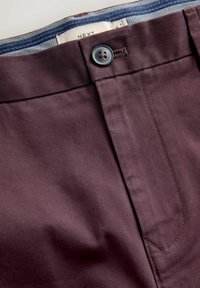 Ciemnofioletowe spodnie o gładkiej fakturze, z zapięciem na guzik oraz kontrastującym wzorzystym paskiem wewnątrz.