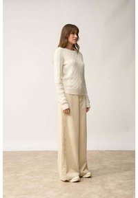Kremowy sweter w warkoczowy splot połączony z szerokimi, ryżowymi spodniami w jasnym beżu. Strój charakteryzuje się luźnym krojem i miękkimi fakturami.