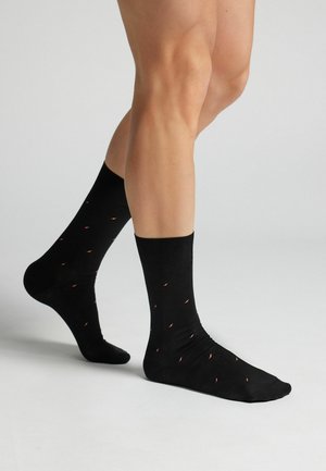 Sorte sokker med en glat tekstur, der har små, farverige chilipeberprint spredt over hele og en ribbet manchet.