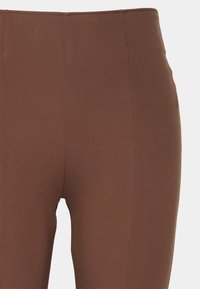 Bruna högmidjade leggings i stretchtyg, med en slät yta och sömdetaljer, åtsittande längs hela benet.