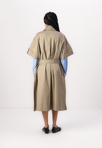 Beige trench coat s krátkymi rukávmi, s opaskom v páse a bočnými vreckami. Má hladkú textúru a prispôsobený strih.