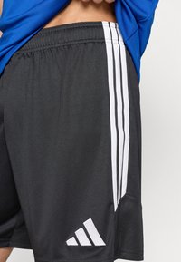 Μαύρο αθλητικό σορτς από ελαφρύ ύφασμα, με τρεις κάθετες λευκές ρίγες και λευκό λογότυπο στο κάτω αριστερό μέρος.