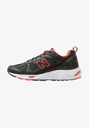 Baskets de sport New Balance noires et rouges avec empeigne en mesh et cuir, semelle blanche rembourrée et fermeture à lacets, vues de côté.