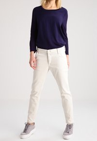 Witte denim jeans met een rechte pasvorm en een vijf-pocket ontwerp, gecombineerd met een marineblauw langmouwshirt en grijze sneakers.