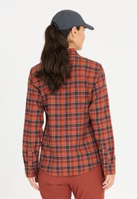 Röd och svart rutigt långärmad skjorta i flanelltyg med en rundad nederkant, knäppta manschetter och en veckdetalj på baksidan.