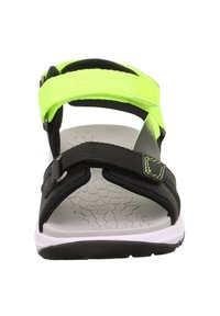 Sandale noire avec des sangles ajustables de couleur néon verte, semelle blanche texturée au motif en nid d'abeille, et semelle en caoutchouc noir.