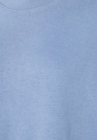 Tissu en coton bleu clair à col rond montrant une texture tricotée et des détails de couture délicats.