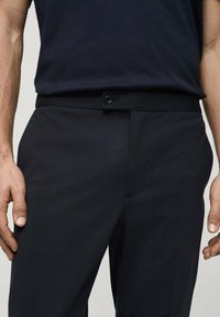 Pantaloni neri con una texture liscia, caratterizzati da passanti per cintura, chiusura con bottone e tasche laterali. Design semplice e vestibilità sartoriale.